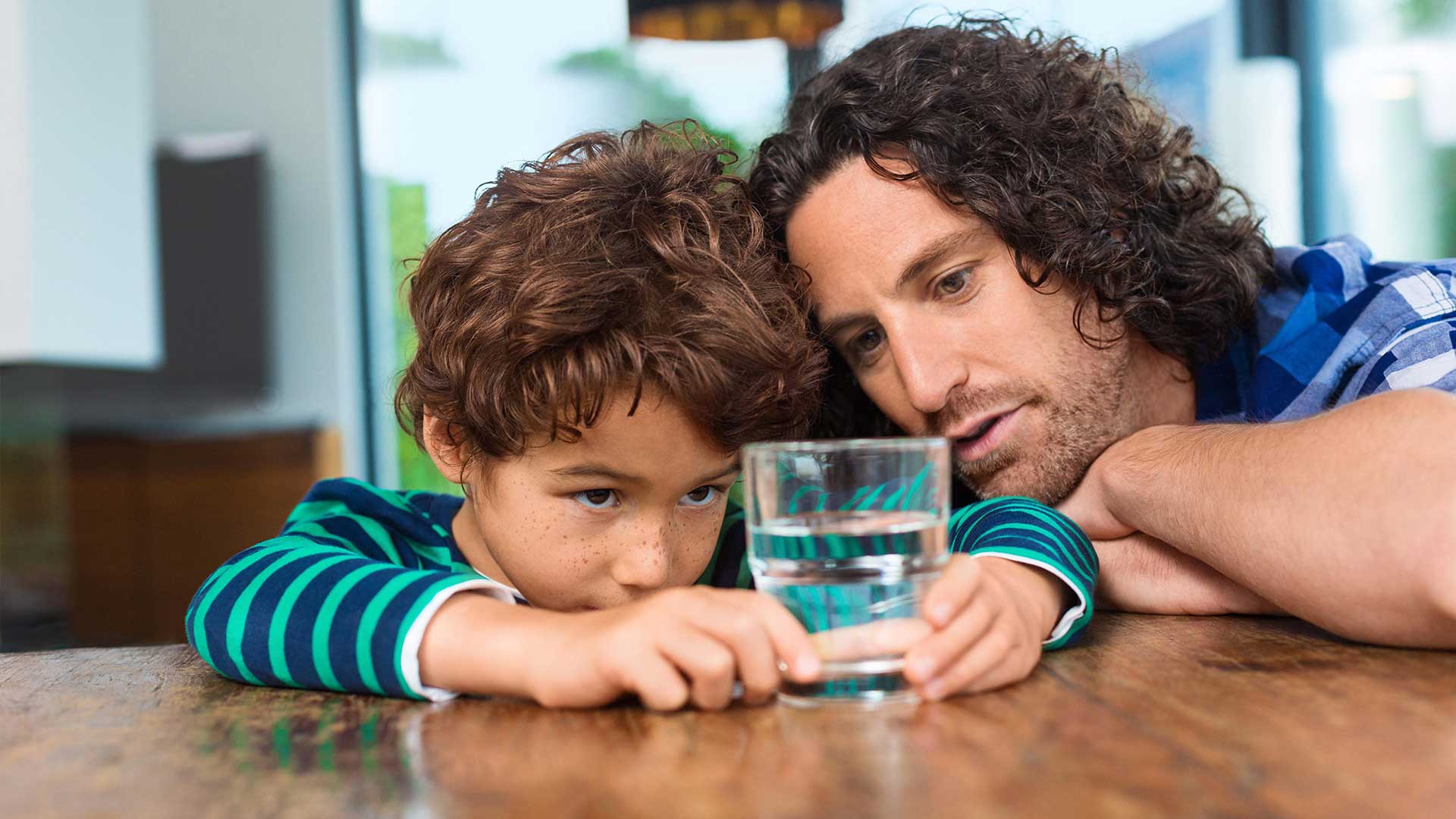 Vater und Sohn schauen auf ein Glas Wasser, das auf einem Tisch steht.